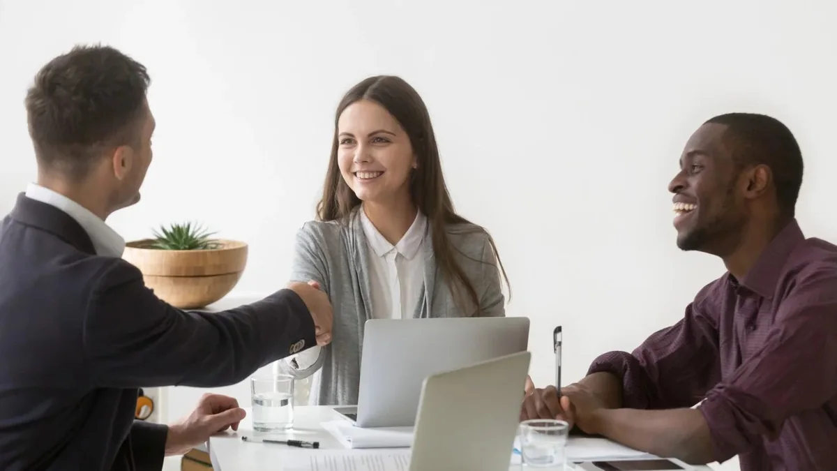 Advisor shaking hands with two clients across a desk during a meeting