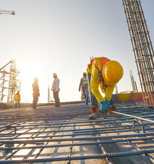 Construction workers in hard hats on a job site at sunrise placing rebar framing