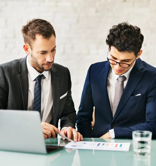 Two professionals in suits reviewing financial charts on a laptop at a desk