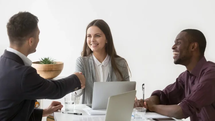 Advisor shaking hands with two clients across a desk during a meeting