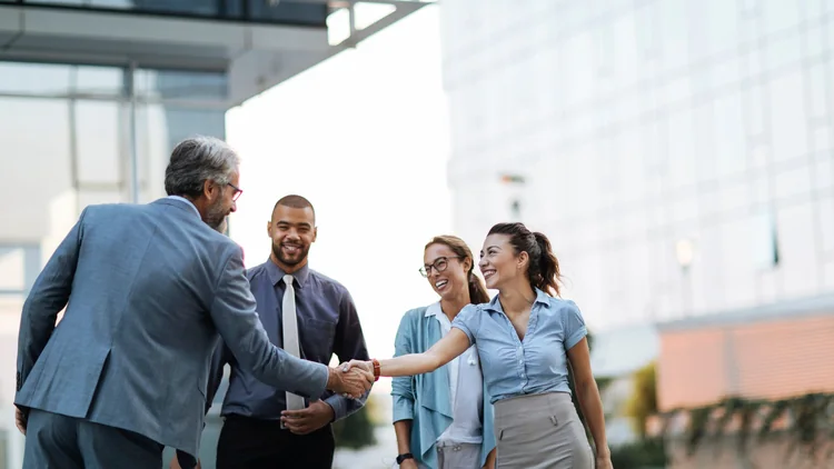 Business professionals shaking hands and smiling outside an office building